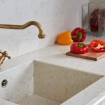 sliced tomatoes and knife on a chopping broad that is over the Akoya countertop that has a built in sink with a gold faucet
