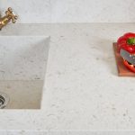 sliced tomatoes and knife on a chopping broad that is over the Akoya countertop that has a built in sink with a gold faucet
