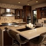 a kitchen a breakfast bar, brown cabinetry, white waterfall edge kitchen island, and a table paired with black swivel stool chairs