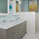 a bathroom with double vanity that has two mirrors and two sinks over the Whitney countertop surface above the taupe wooden bath cabinetry against the white tiled floor and blue painted walls