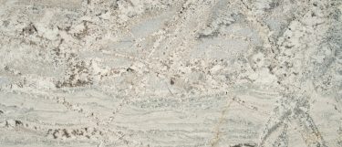 a Monte Cristo countertop surface that has a pearly white background with streaks and veining patterns in midnight blues, grays, yellow, and earth tones