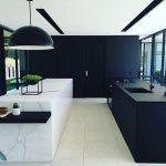 a kitchen with a black wall surface contrasting the white ceiling and floor, an Absolute Black kitchen counter with black faucet and sink, and a white stone kitchen island