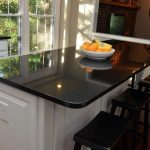 a bowl of fruits over the breakfast bar that has Absolute Black countertops and white base paired with black bar stools