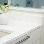 a white flower vase by the sink over the morning frost countertop above the white cabinet drawer base