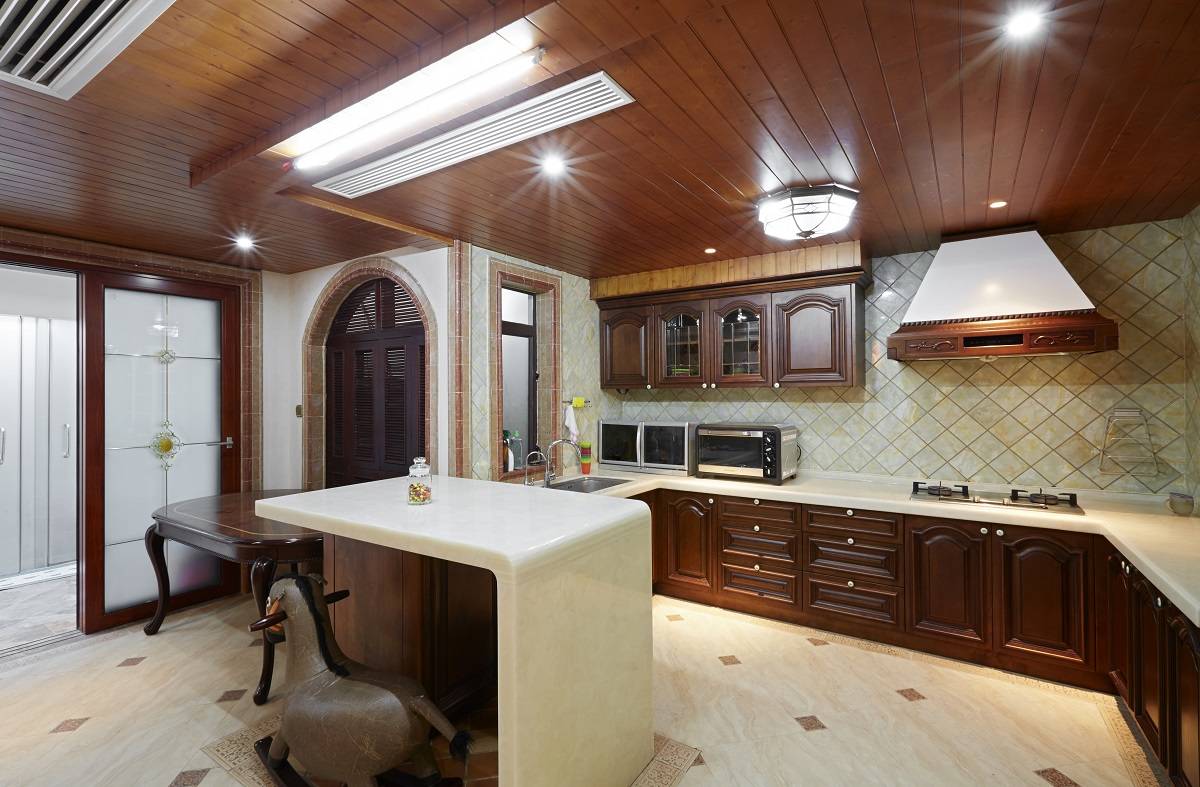 a classic look kitchen with dark ceiling, cabinets, tables, and doors in dark brown paired with the countertops and flooring in beige