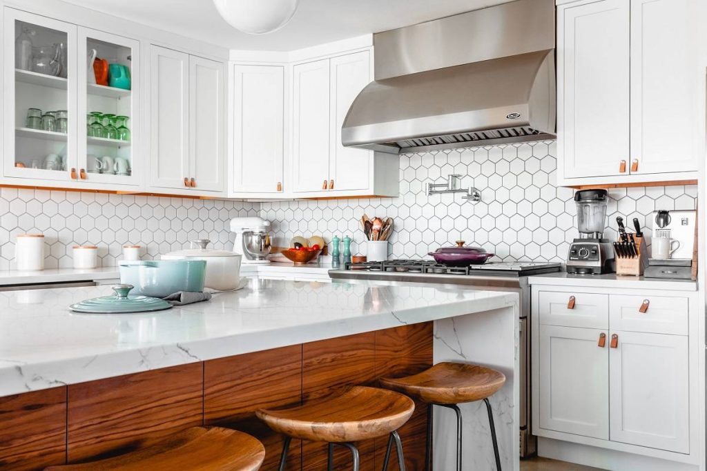 A white kitchen with brown accents that features white cabinets, a white countertop, and a hexagonal backsplash