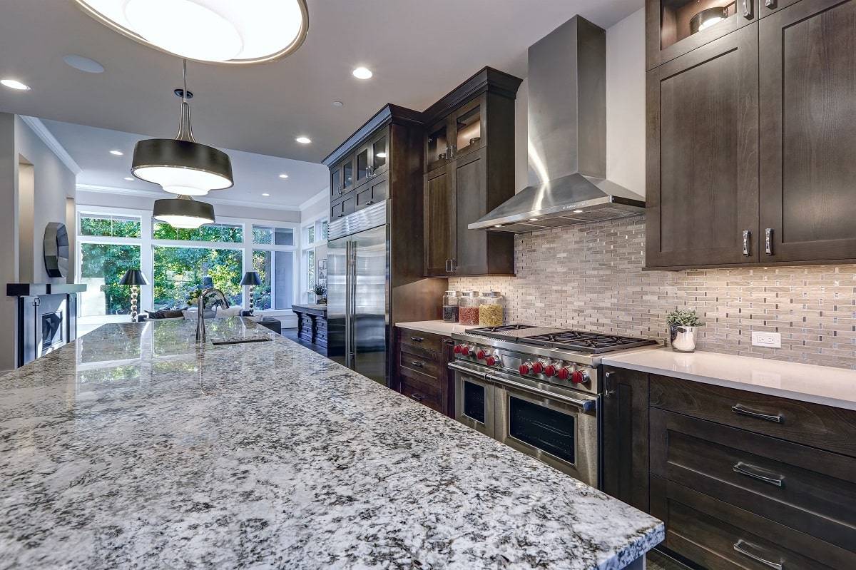 a kitchen with a white countertop with black flecks and veining that complements the dark brown cabinets and black lighting fixtures 