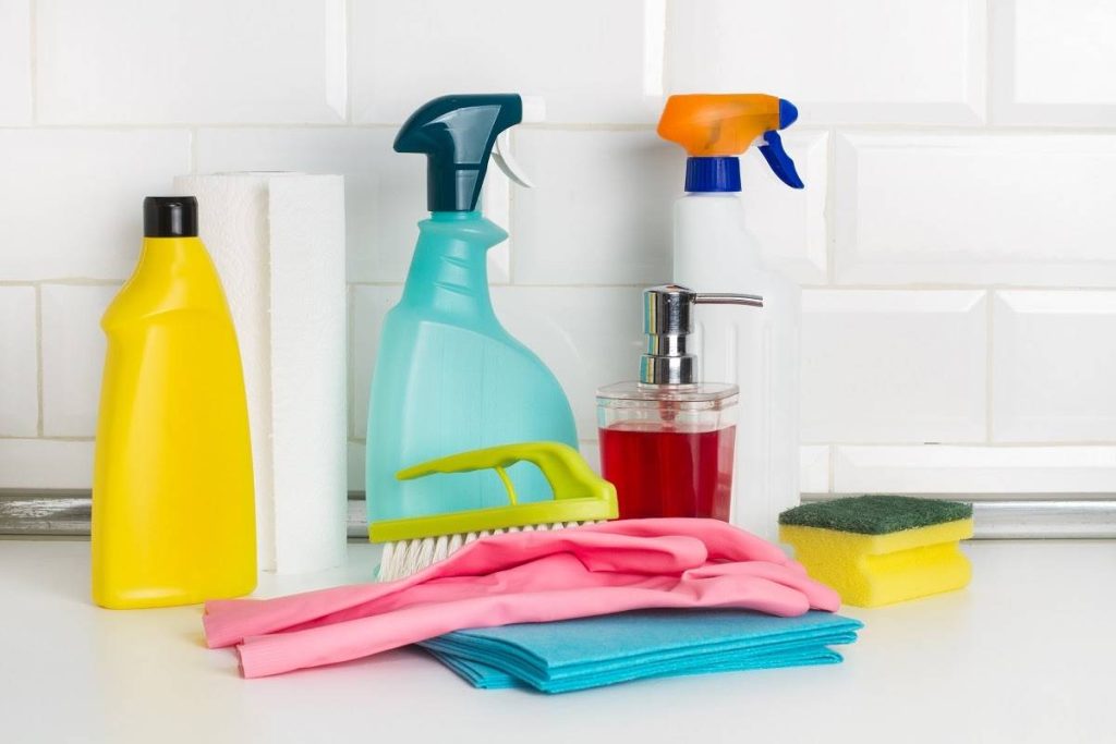 cleaning materials with cleaning bottles, brushes, gloves, and sponge over the white countertop