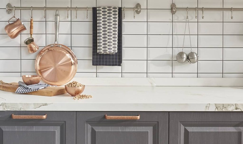a white quartz countertop by the rectangular backsplash in white and above the gray cabinets