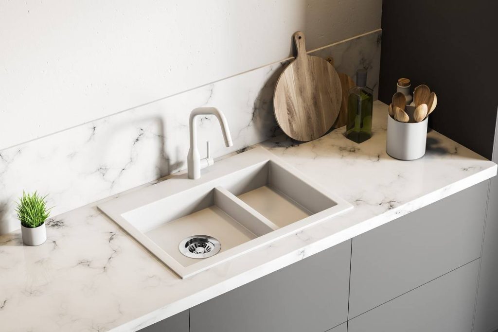 a clean marble-finish counter with a white sink and faucet and wooden cooking utensils and chopping board