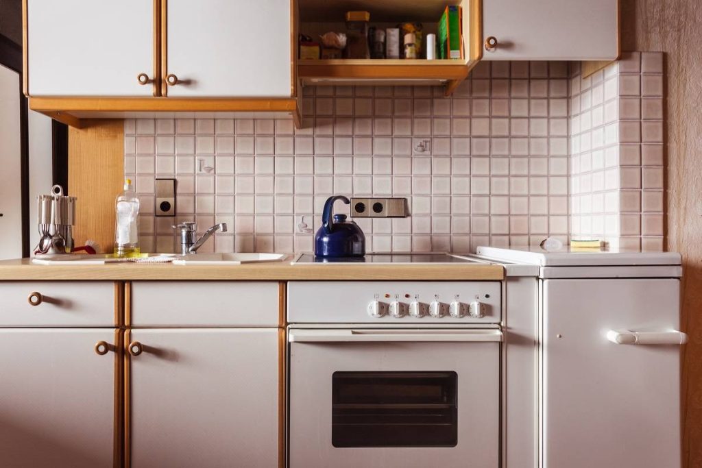 interior of an old, simple kitchen with an old-style white backsplash and white cabinets with brown accents