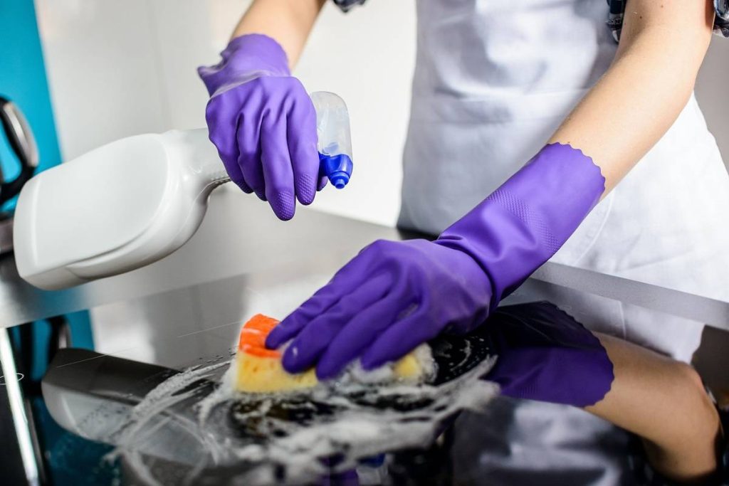 a woman using a sponge and cleaning solution spray to scrub the black kitchen countertop while wearing protective rubber gloves