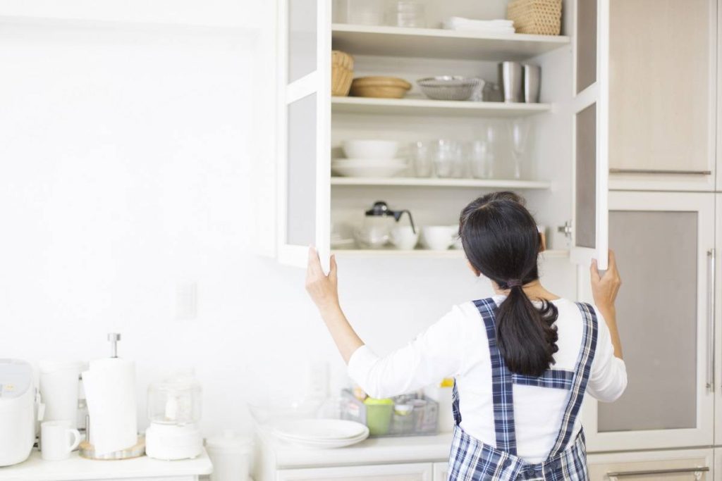 a woman opening a white kitchen cabinet that serves as a storage for plates, glasses, and bowls