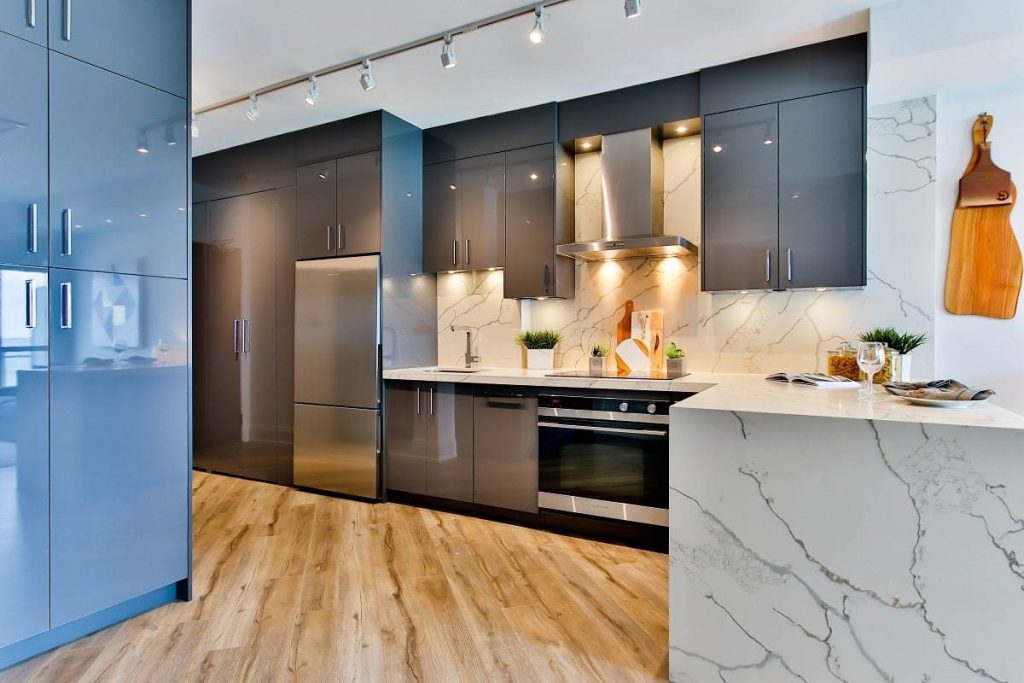 a kitchen with glossy cabinetry in gray and blue with white countertops against the hardwood floor