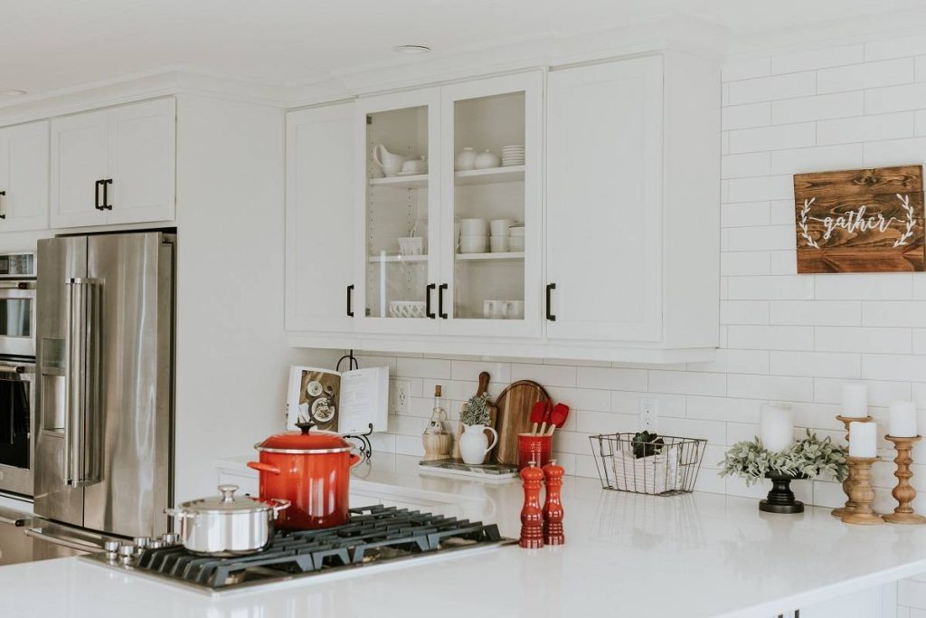 a kitchen corner with white countertops and cabinets, red kitchen wares, candles on pillar stands, and other appliances