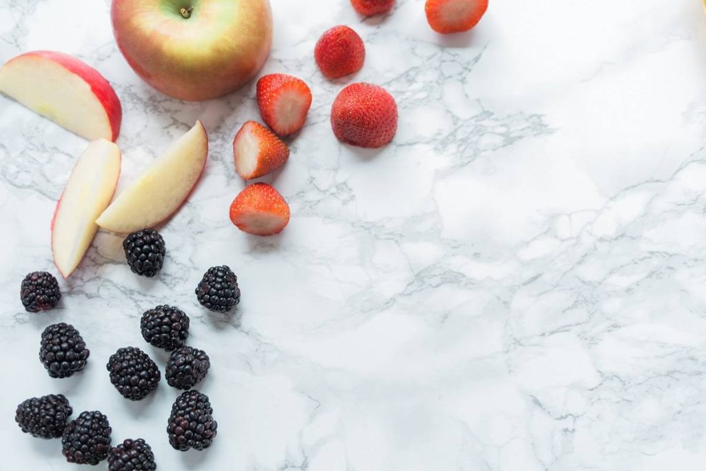 apples and berries scattered on a white marble countertop