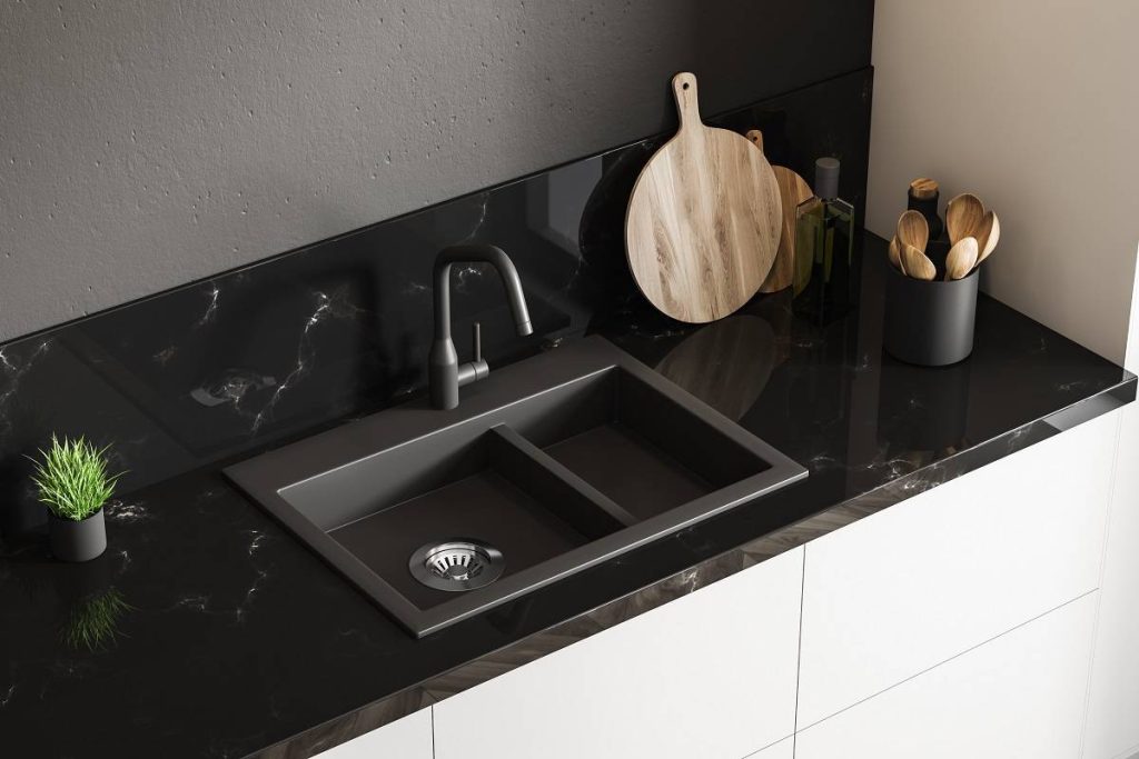 black sink and wooden utensils above the black marble countertop with a white cabinet base