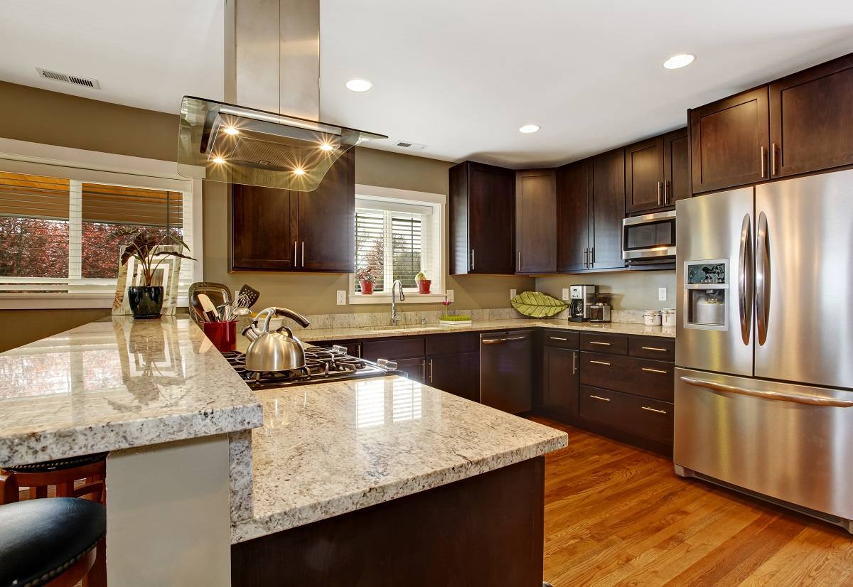 a dark brown kitchen with white countertops, stainless steel appliances, dark wood cabinets, and a hardwood floor