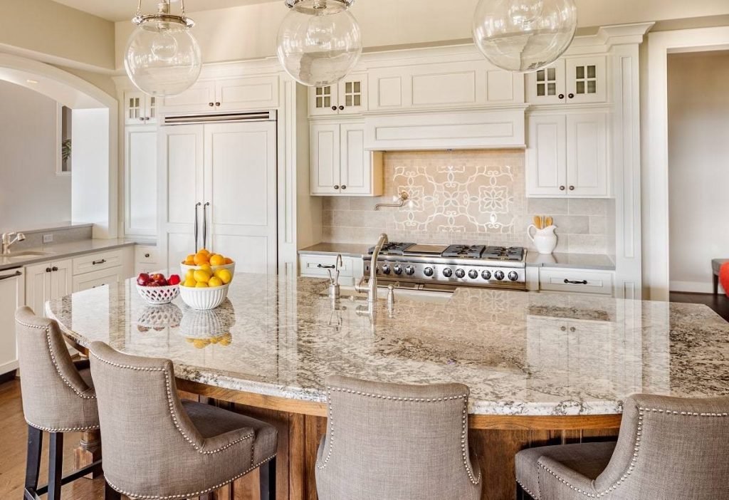 a kitchen with a beige countertop and breakfast bar island with cushioned chairs and white cabinetry