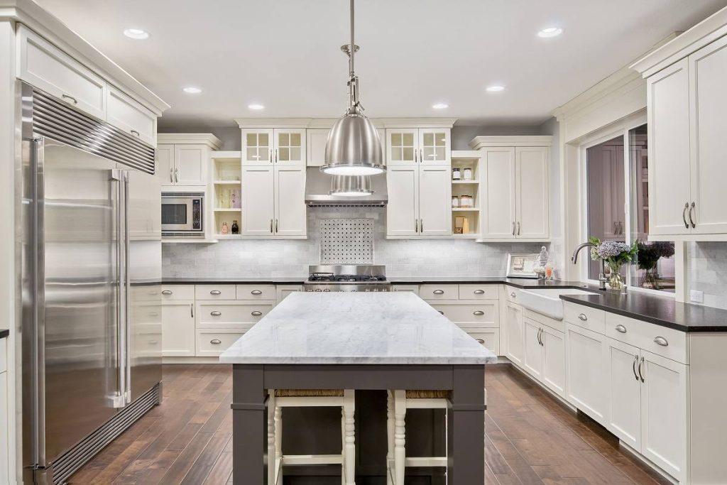 a kitchen interior featuring white cabinetry topped with black countertops, and a kitchen island in gray base and white countertop, hardwood floors, and stainless appliances
