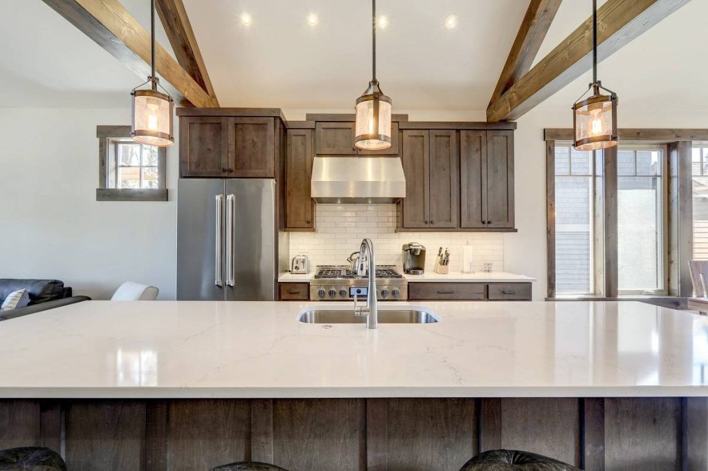 a modern and rustic kitchen with wooden cabinets, white countertops, pendant lights, stainless steel appliances, and a vaulted ceiling