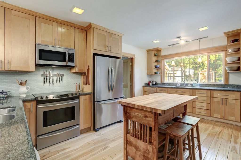 a nice country home wood kitchen with wooden island, wooden cabinetry, black countertops, and hardwood floor