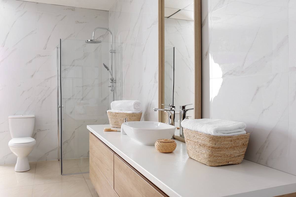 a large mirror, vessel sink, and towels on a basket above the white countertop over the light brown wooden drawers
