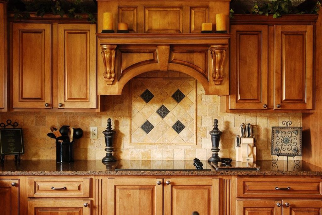a vintage style cabinetry with old beige backsplash, vintage furniture, brown countertop, black kitchen ware, candles, and wooden cabinetry